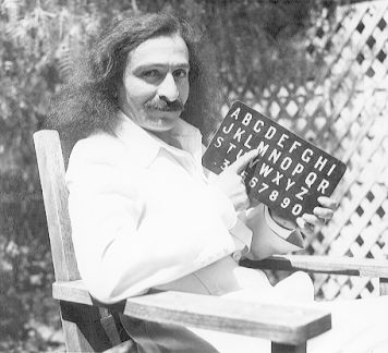 Meher Baba sitting in a garden in Hollywood in 1932 points to a letter on his alphabet board